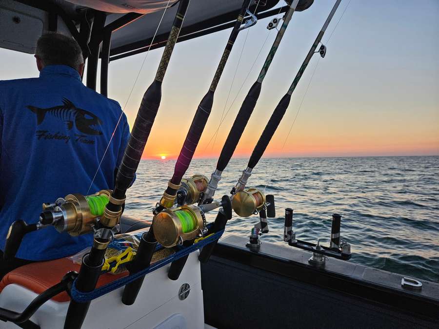 Canne e mulinelli pronti sul gommone all’alba, con un pescatore di spalle