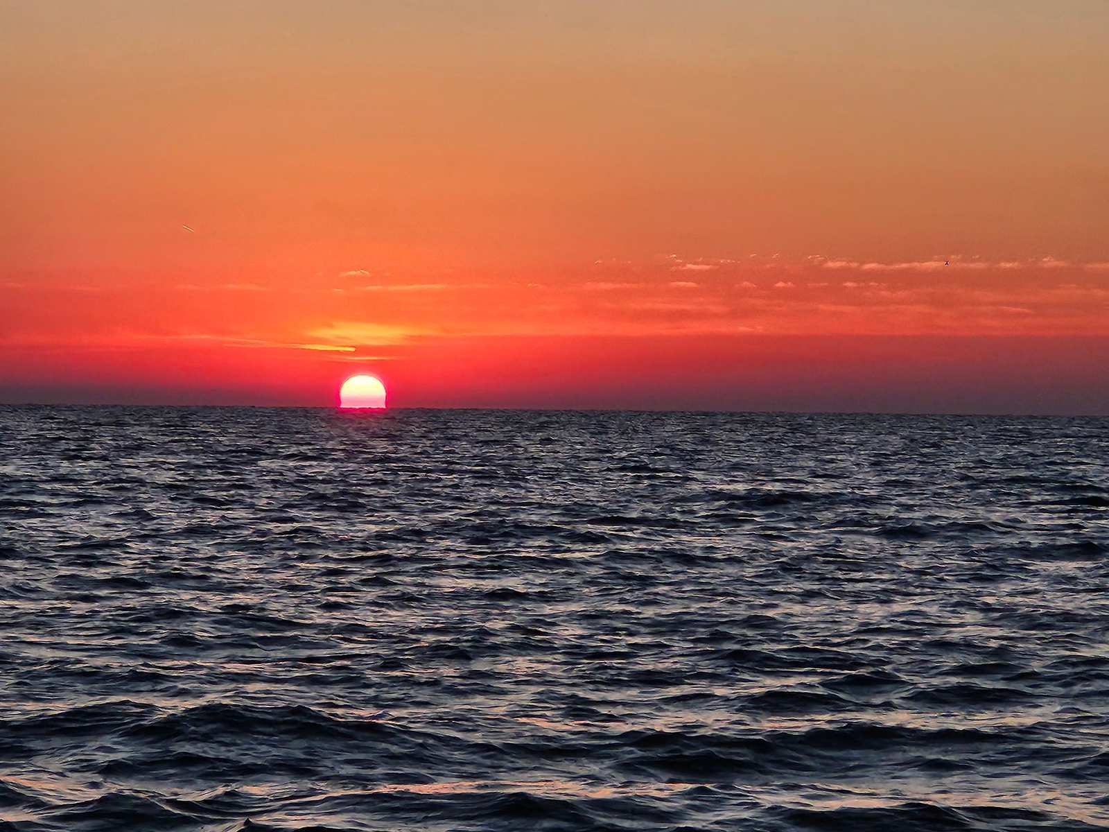 Il sole che sorge sul mare, cielo arancio e acqua scura