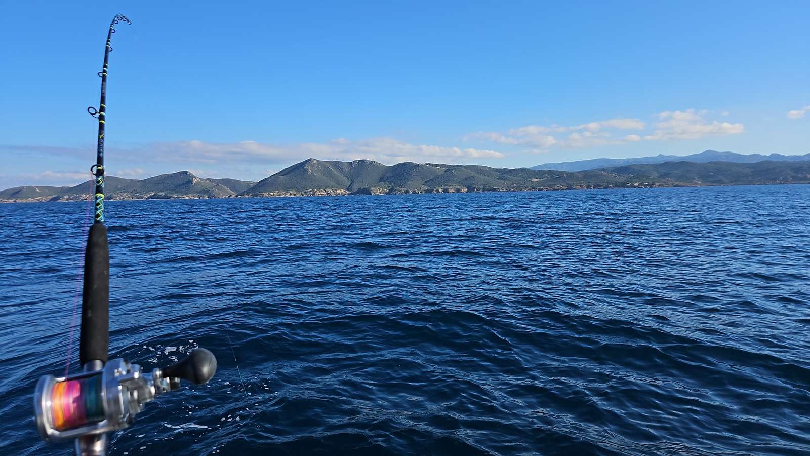 Canna e mulinello pronti sul gommone, con il mare e la costa sullo sfondo