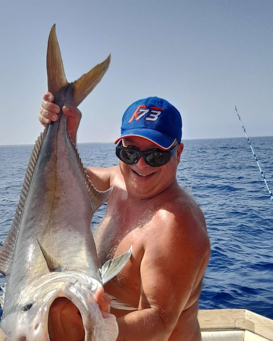 Un pescatore solleva una grossa cattura contro il cielo blu