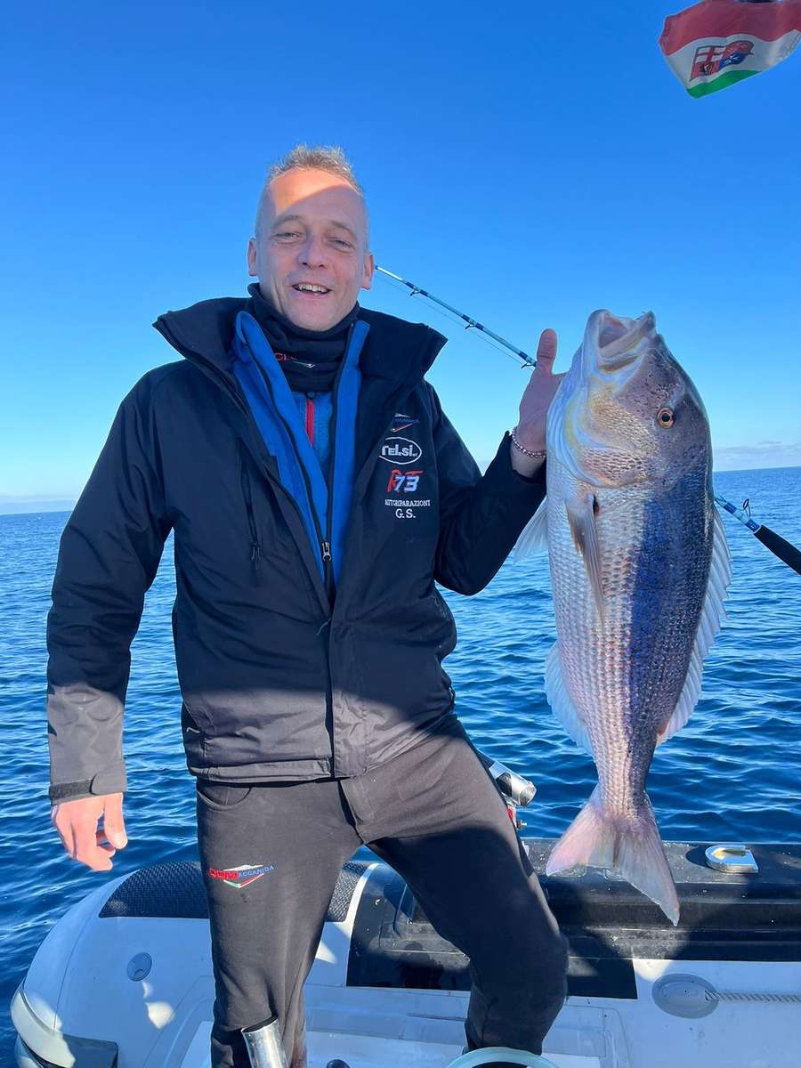 Un pescatore sorridente con la giacca pesante solleva una grossa cattura sul gommone