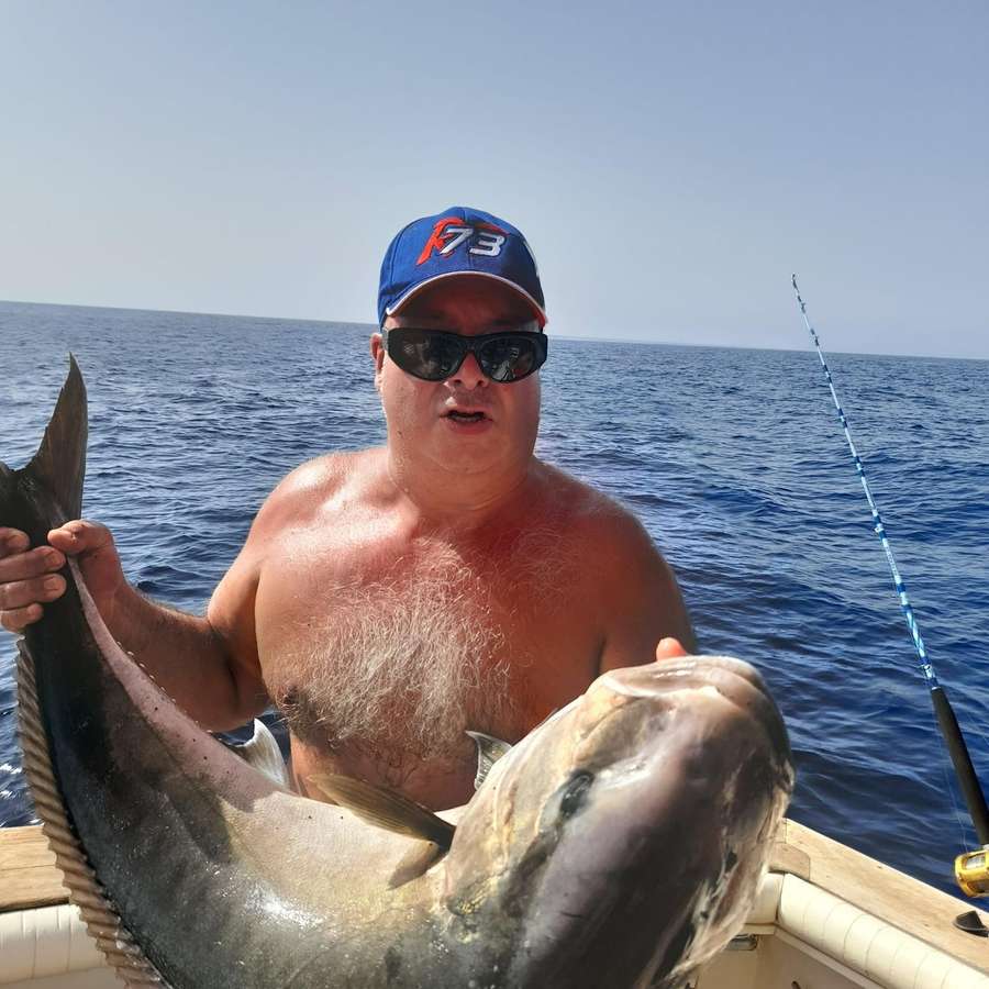Il pescatore con il cappellino solleva una grossa cattura con due mani, sul mare blu