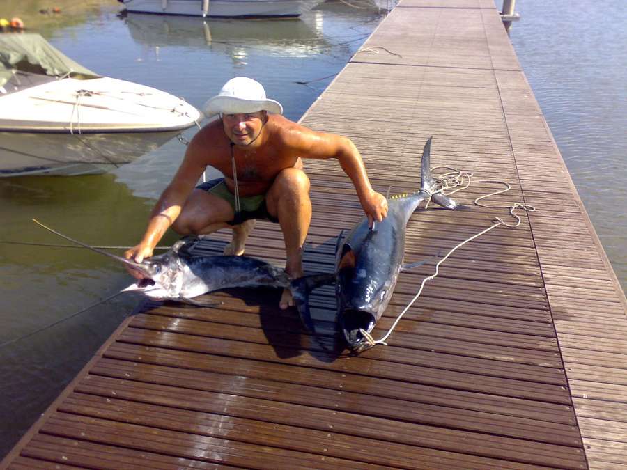 Due grosse catture su un pontile di legno, con il pescatore accovacciato