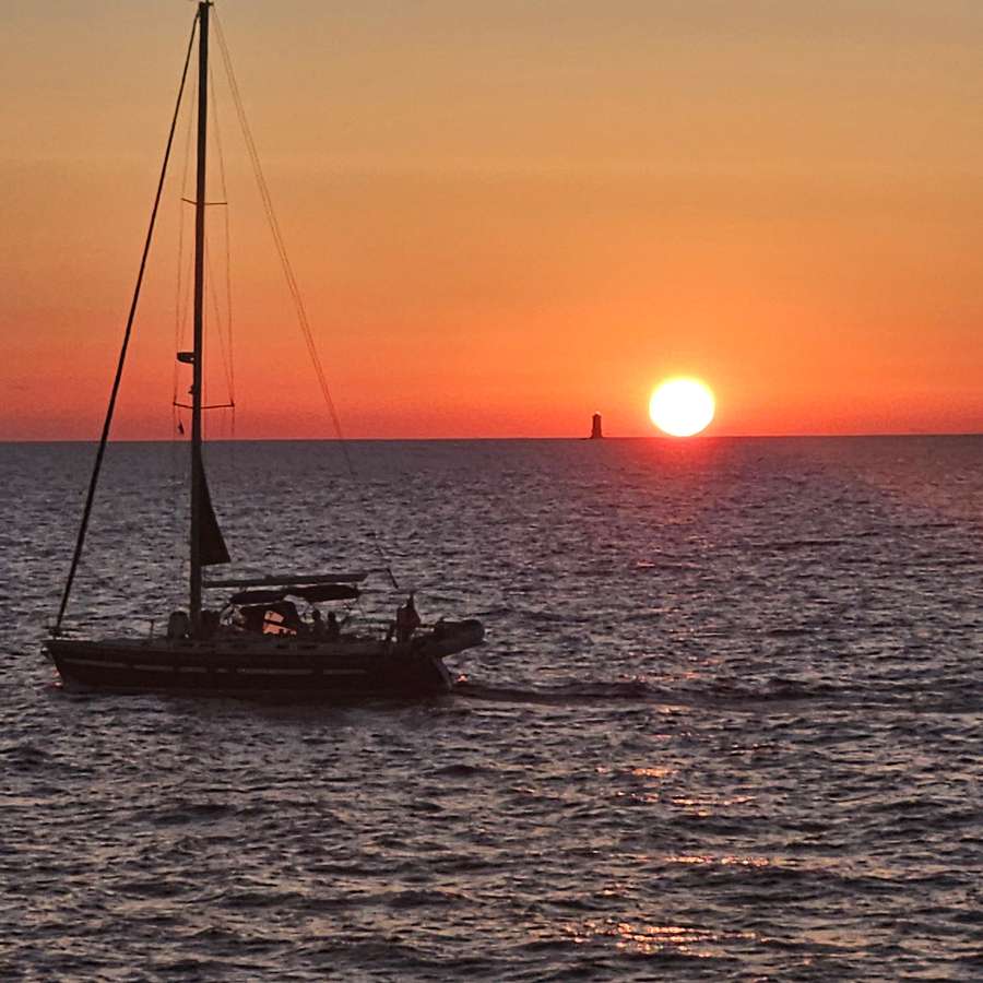 Tramonto in mare con una barca a vela controluce