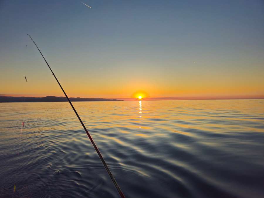 Canna da pesca sul mare piatto al tramonto