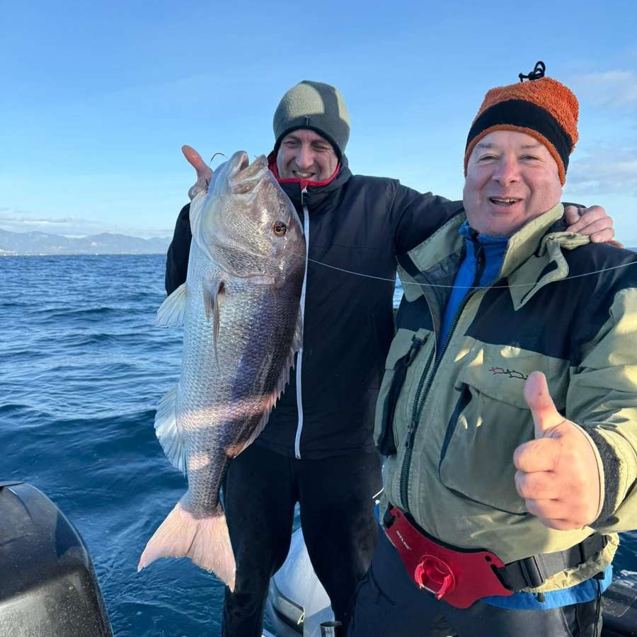 Due pescatori sorridenti sul gommone con una grossa cattura sollevata