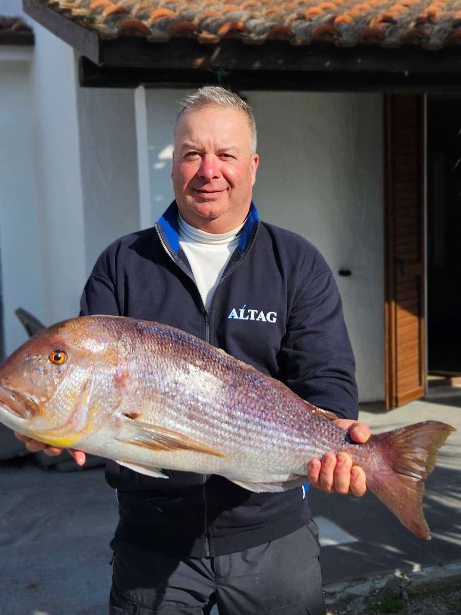 Un pescatore sorridente davanti a casa solleva una grossa cattura a due mani