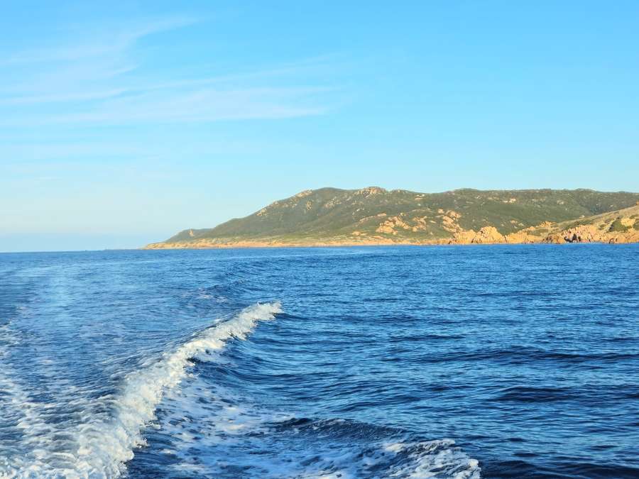La scia in curva sul mare blu, con un promontorio verde e roccioso in fondo