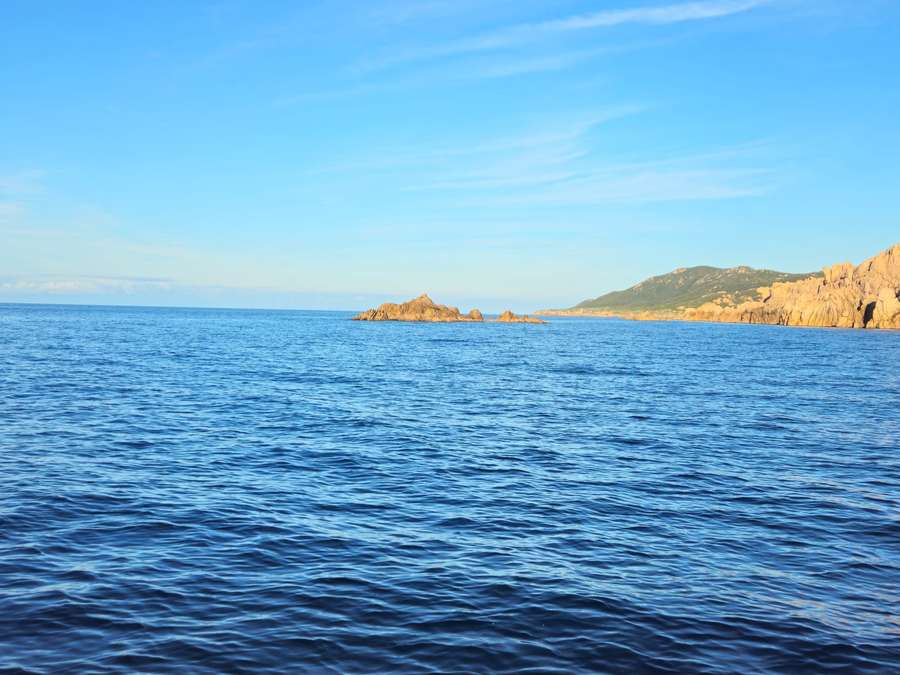 Mare blu increspato con uno scoglio isolato e un promontorio roccioso a destra
