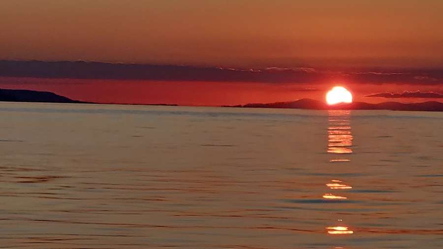 Il sole che tramonta dietro le colline, riflesso sul mare calmo